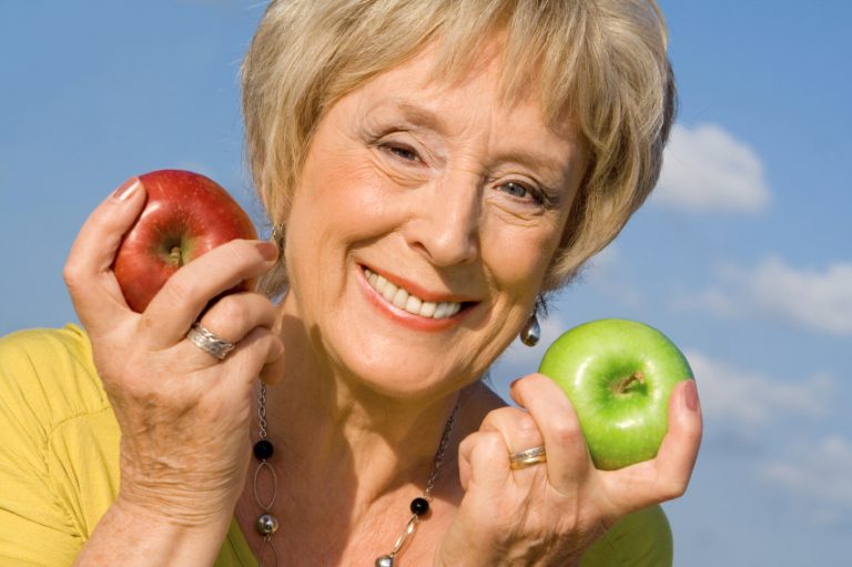 A mature woman smiling while holding two apples.