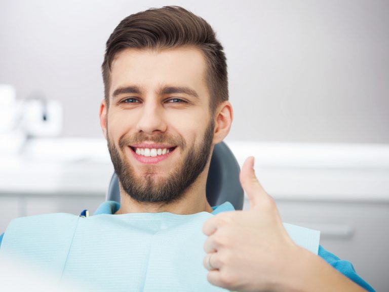 A young man holding his thumb up during his teeth whitening treatment in OKC.