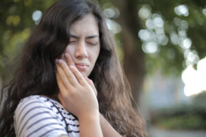 A young woman clutching her jaw in pain after a dental injury.